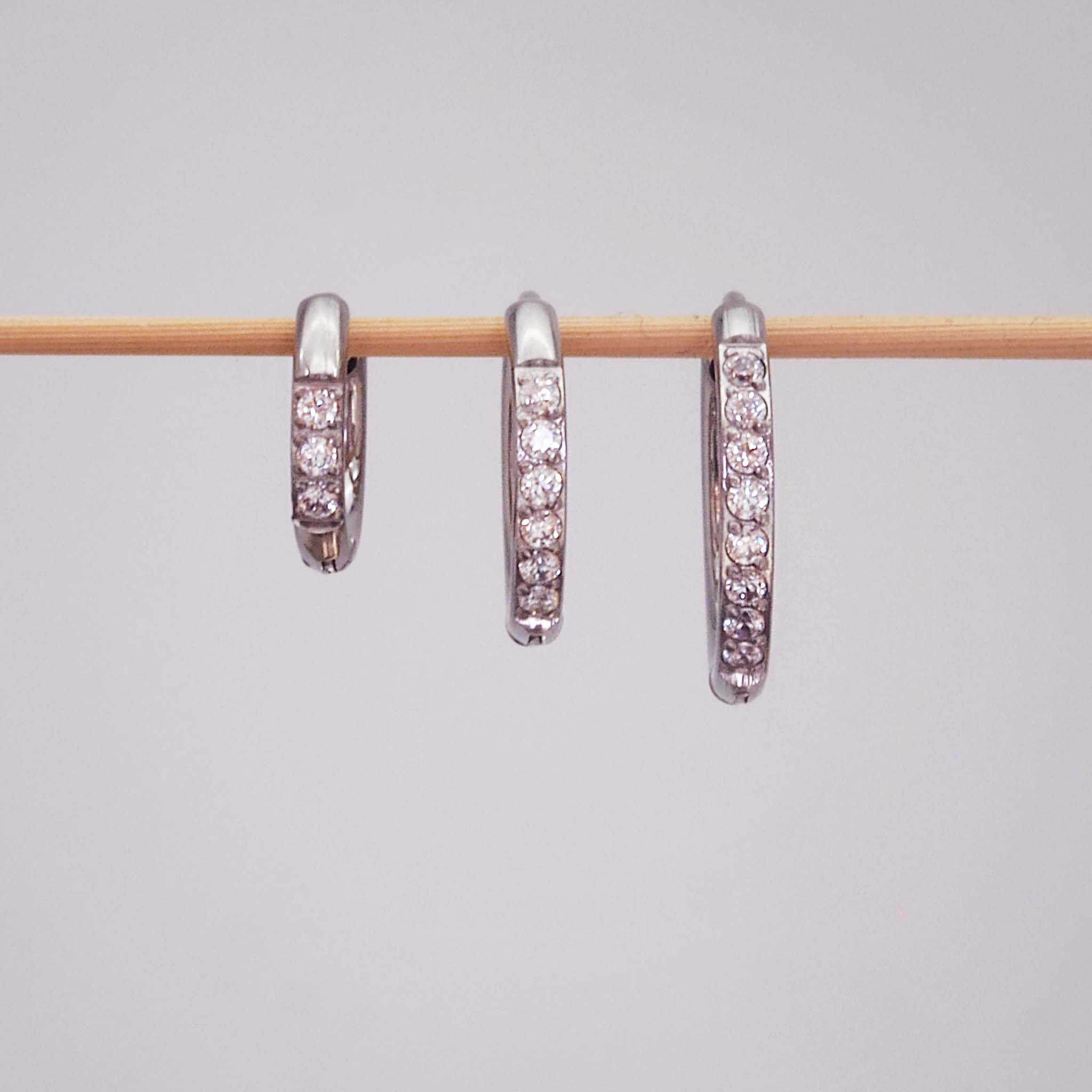 Three stainless steel waterproof pavé silver hoop earrings in three different hoop huggie earring sizes