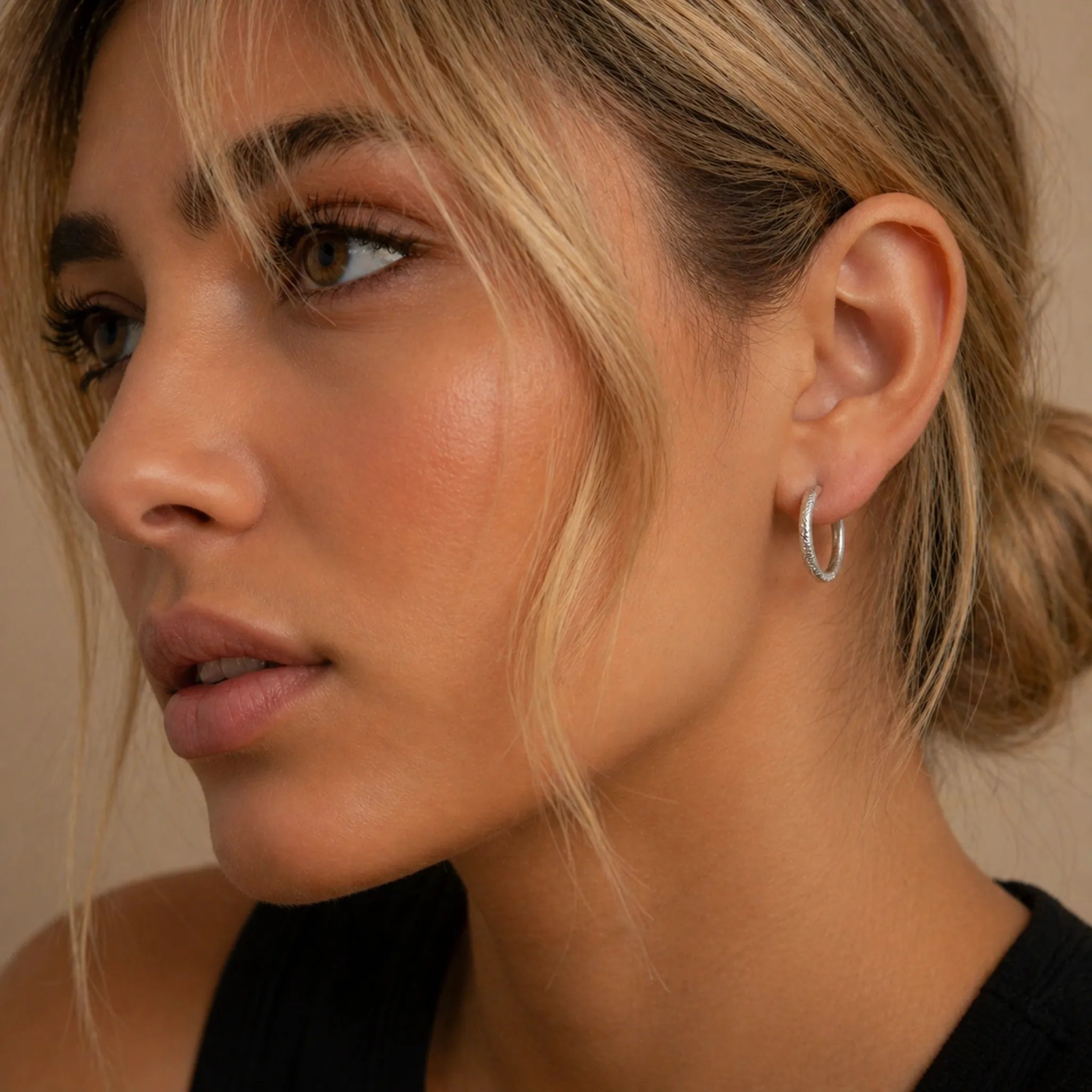 Close-up of a woman wearing a stainless steel waterproof silver hoop earring against a neutral background