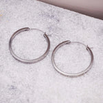 Pair of silver hoop earrings on a textured surface