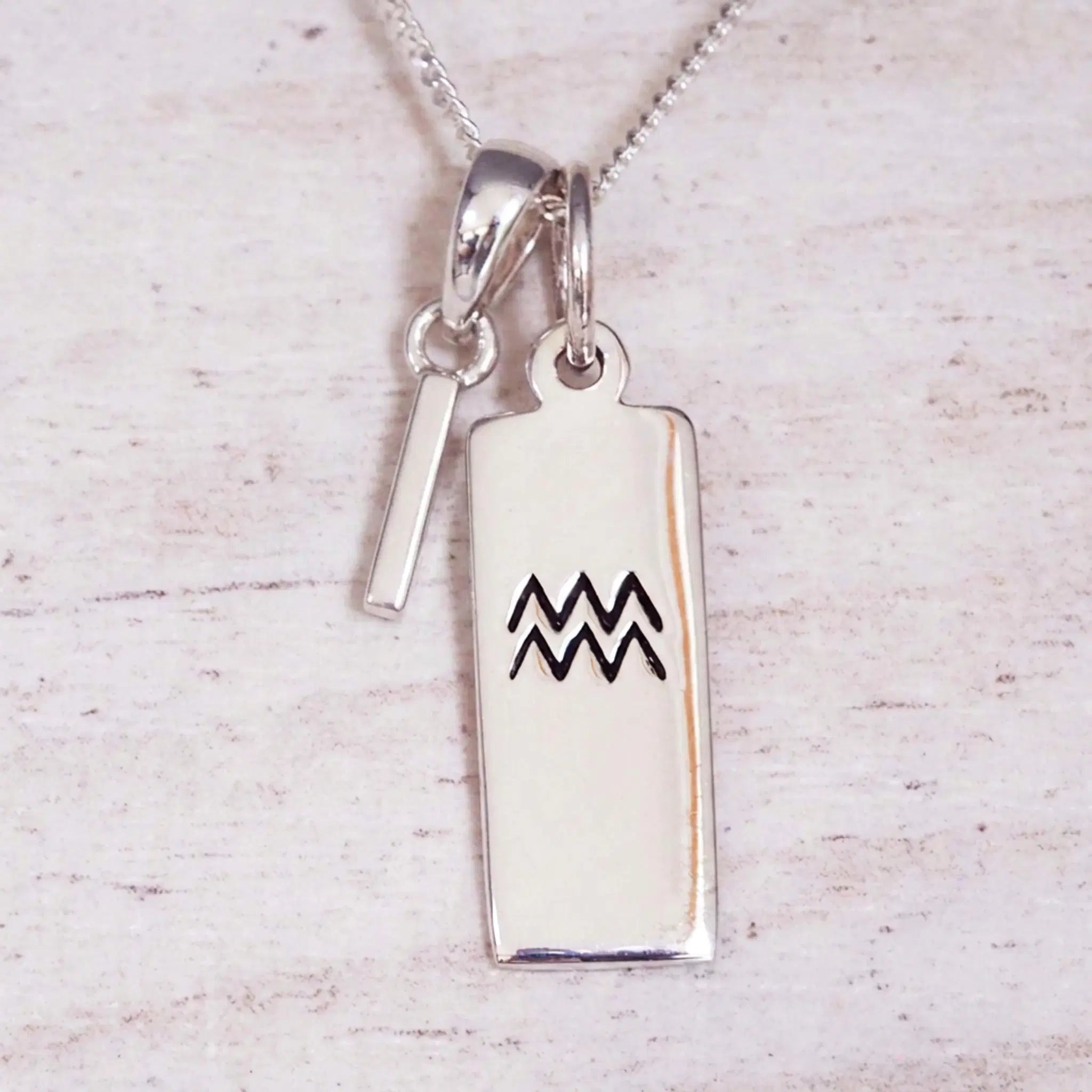 Sterling Silver I Initial and Aquarius Necklace on a fine silver chain against a light wooden background