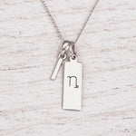 sterling silver initial I pendant and capricorn necklace on a fine silver chain against a light wooden background