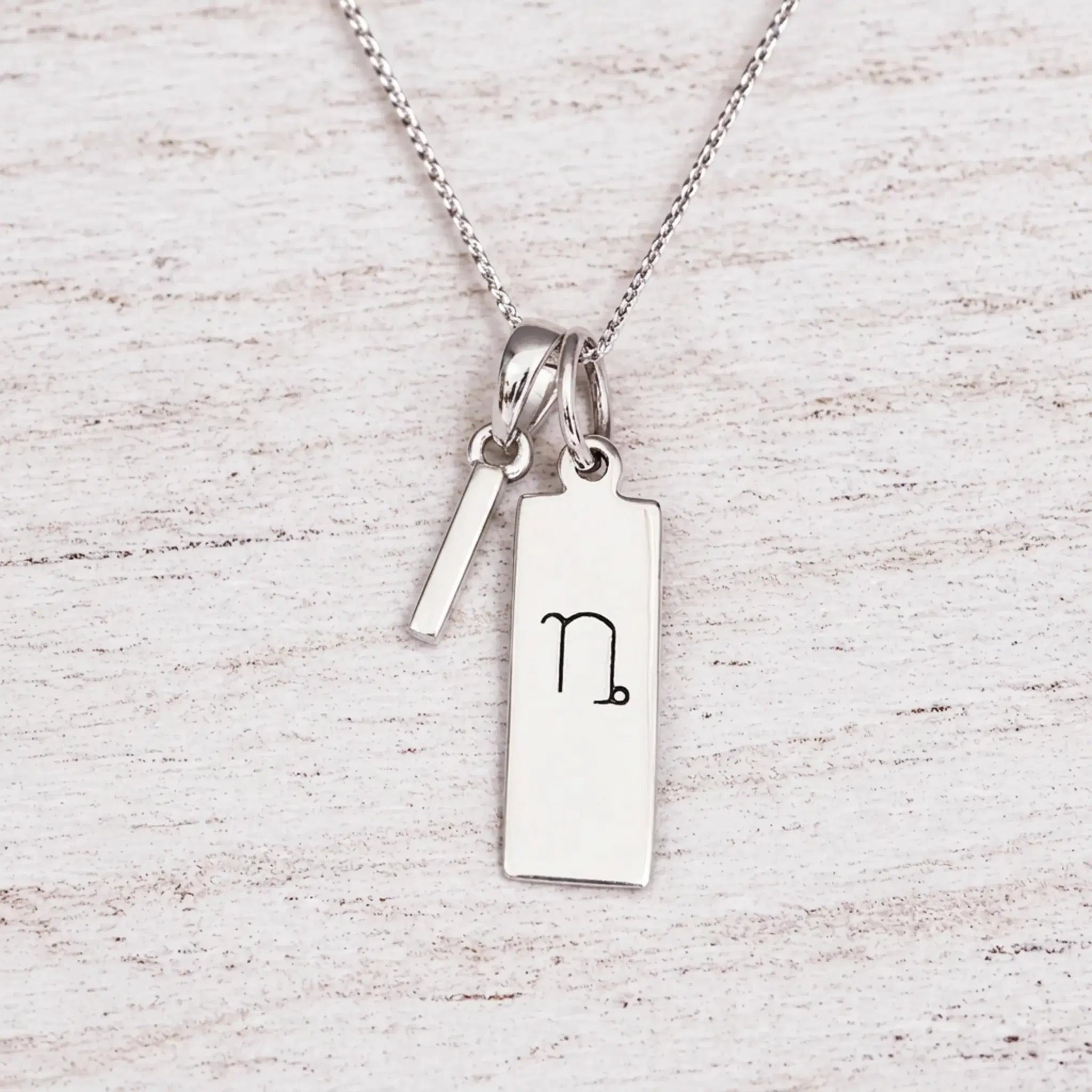 sterling silver initial I pendant and capricorn necklace on a fine silver chain against a light wooden background