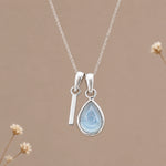 Sterling silver initial I and November natural blue topaz necklace on a taupe background with sparse ivory flowers