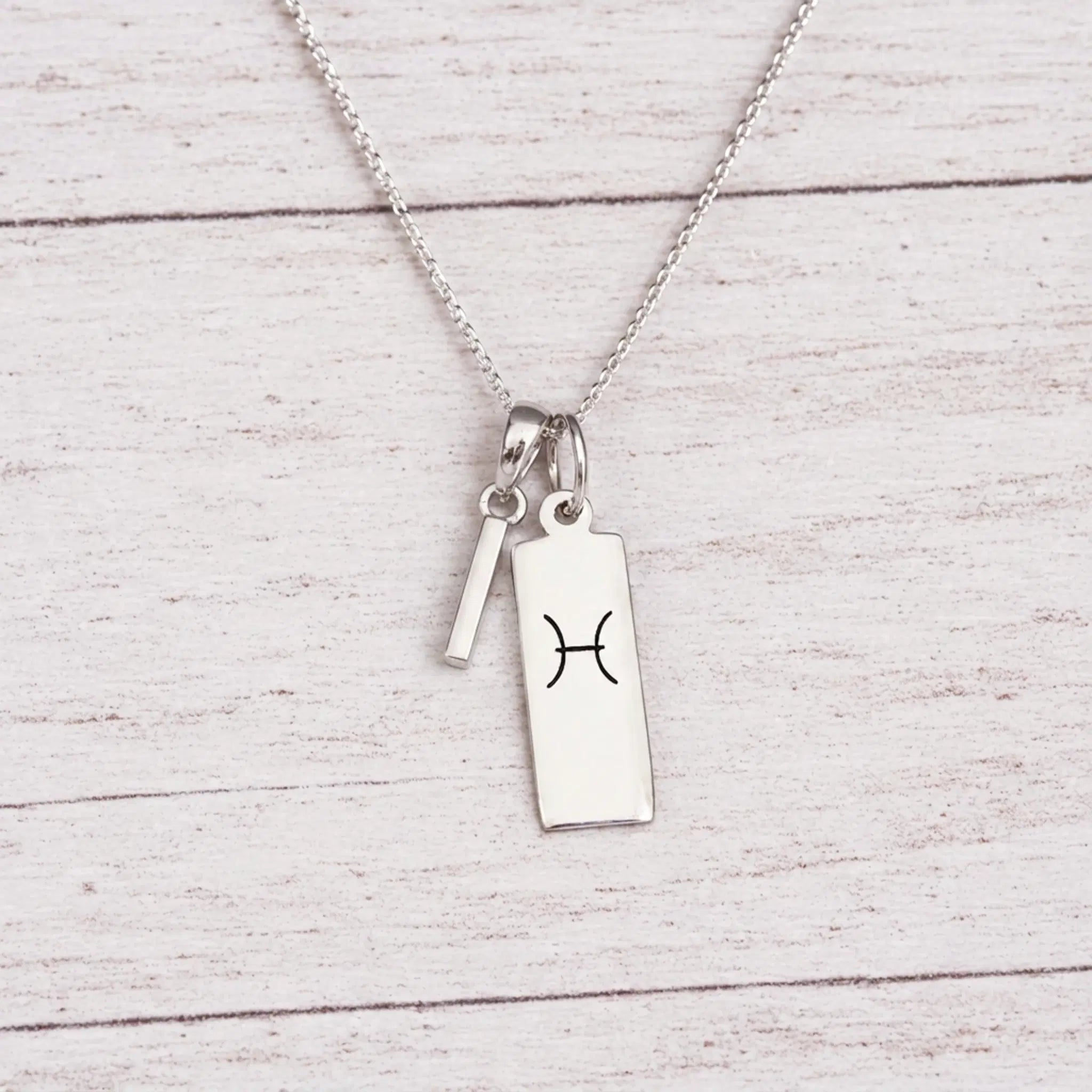  sterling silver I initial Pisces Necklace on a fine silver chain against a light wooden background