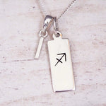 sterling silver initial i sagittarius zodiac star sign pendant necklace against a light wooden background