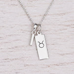 Sterling silver I initial Pendant and Taurus Necklace on a fine silver chain on a light wooden background