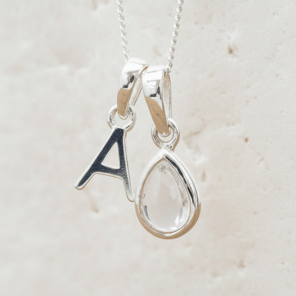 Silver necklace with 'A' initial pendant and teardrop-shaped Herkimer Quartz Crystal hanging above a wooden table