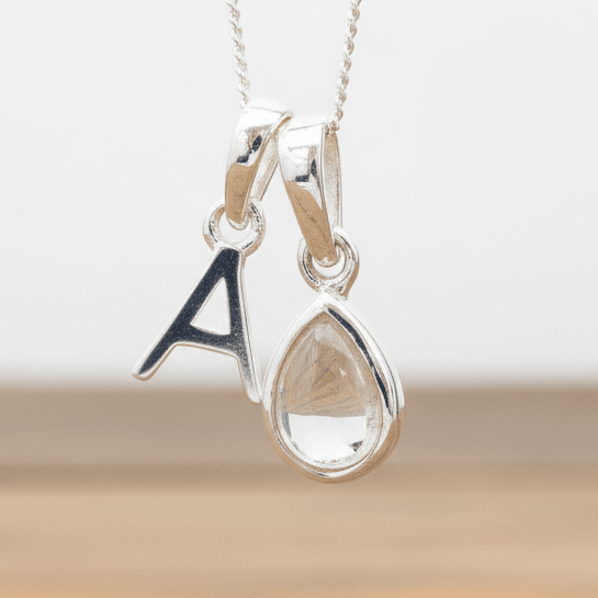 Silver necklace with 'A' initial pendant and teardrop-shaped Herkimer Quartz Crystal hanging above a wooden table