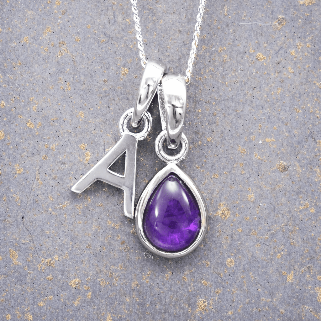 Silver necklace with a purple teardrop february birthstone amethyst pendant and letter 'A' charm on a textured gray background.