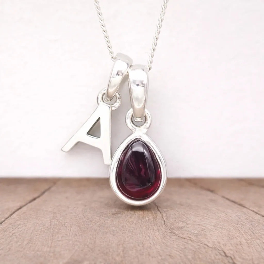 Silver Initial A necklace with a teardrop-shaped red Garnet gemstone pendant on a light wooden surface.