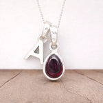 Silver Initial A necklace with a teardrop-shaped red Garnet gemstone pendant on a light wooden surface.