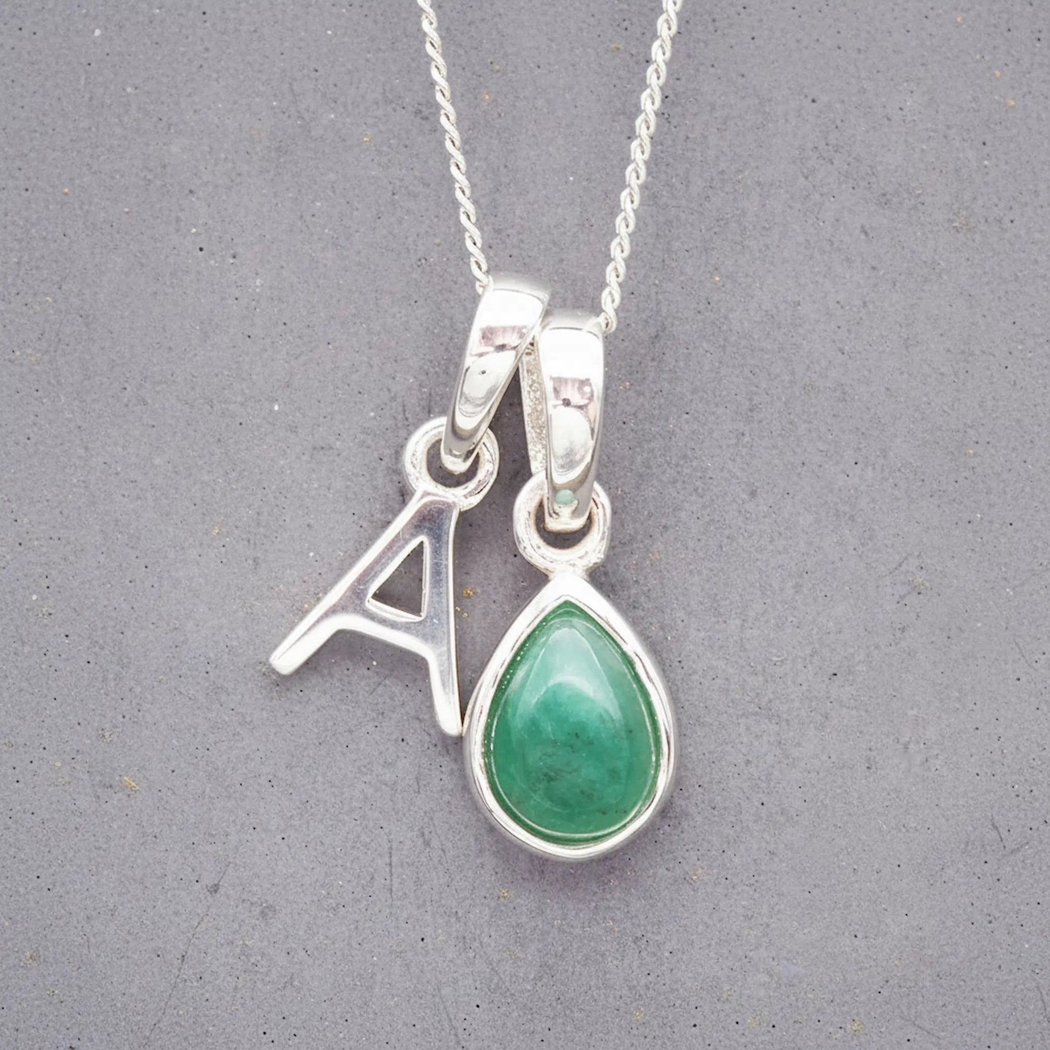 Sterling Silver double pendant necklace with a green teardrop may birthstone emerald pendant and letter 'A' charm on a grey background