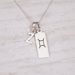 Sterling Silver double pendant necklace with a rectangular gemini zodiac glyph pendant and a upper case block letter 'Z' pendant on a light wooden background.