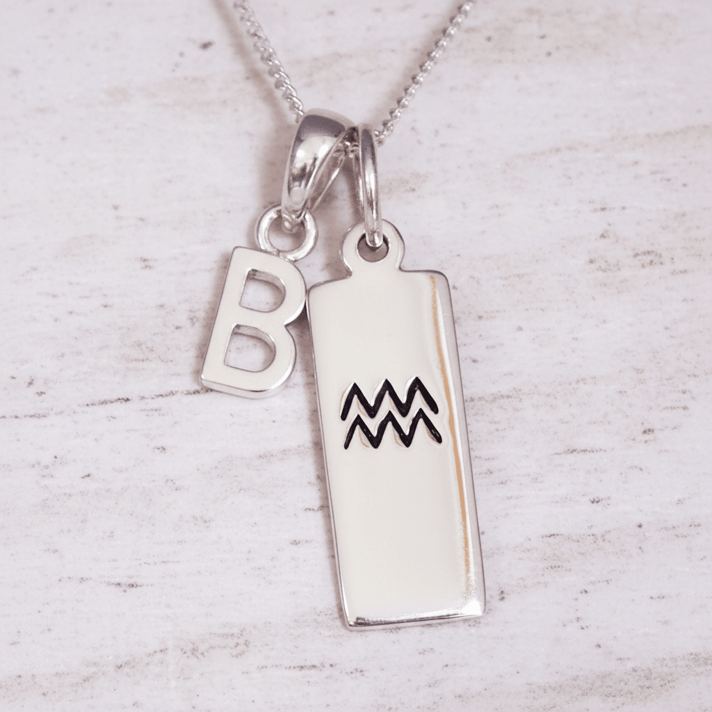 Silver necklace with 'B' pendant and Aquarius zodiac symbol pendant on a light wooden background