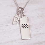 Silver necklace with 'B' pendant and Aquarius zodiac symbol pendant on a light wooden background