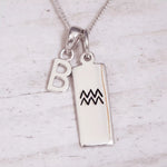 Silver necklace with 'B' pendant and Aquarius zodiac symbol pendant on a light wooden background
