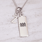 Silver pendant with 'Z' and Aquarius symbol on a light wooden background