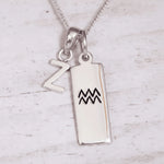 Silver pendant with 'Z' and Aquarius symbol on a light wooden background