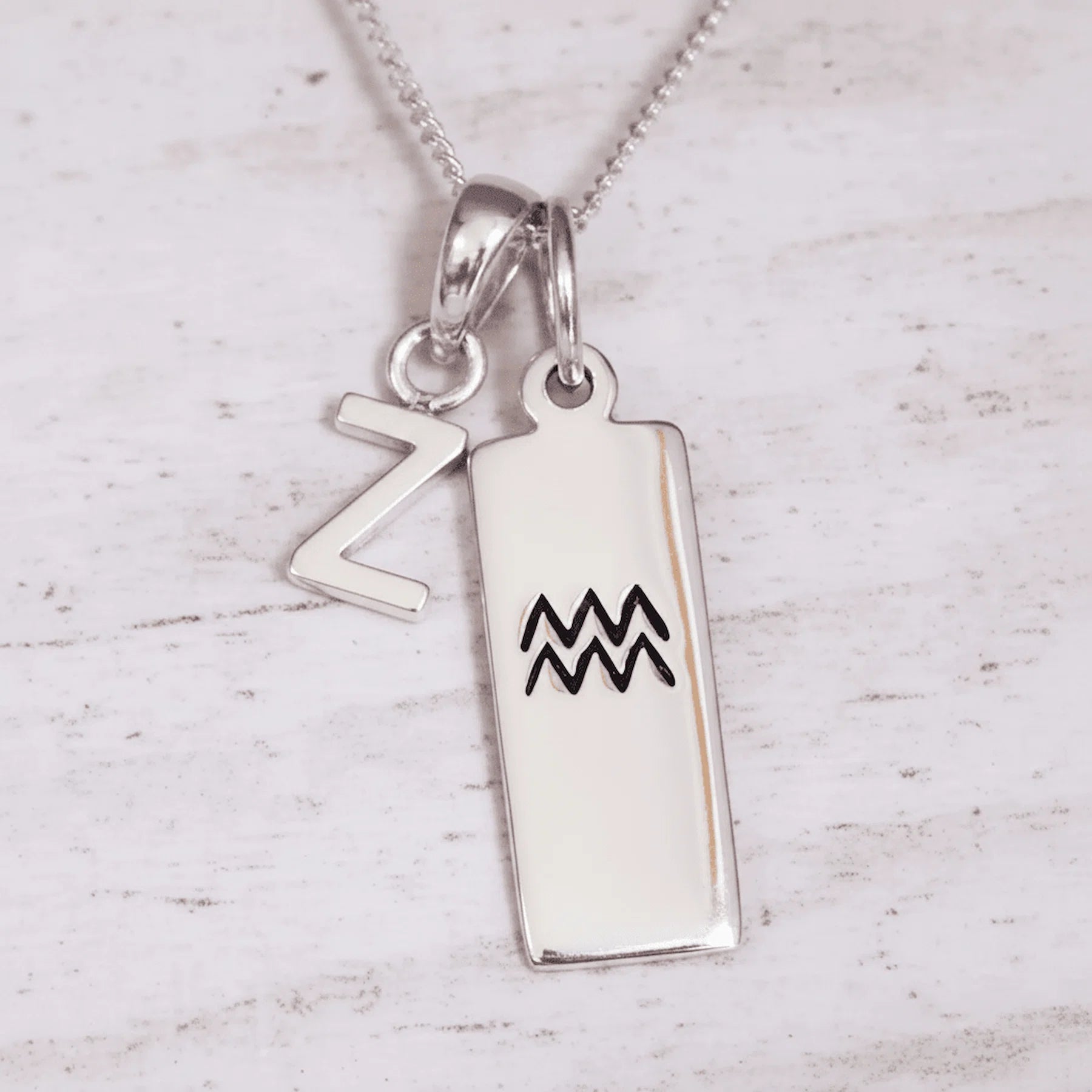 Silver pendant with 'Z' and Aquarius symbol on a light wooden background