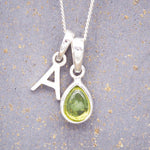 Silver necklace with a 'A' initial pendant and a green teardrop august birthstone peridot pendant on a grey background