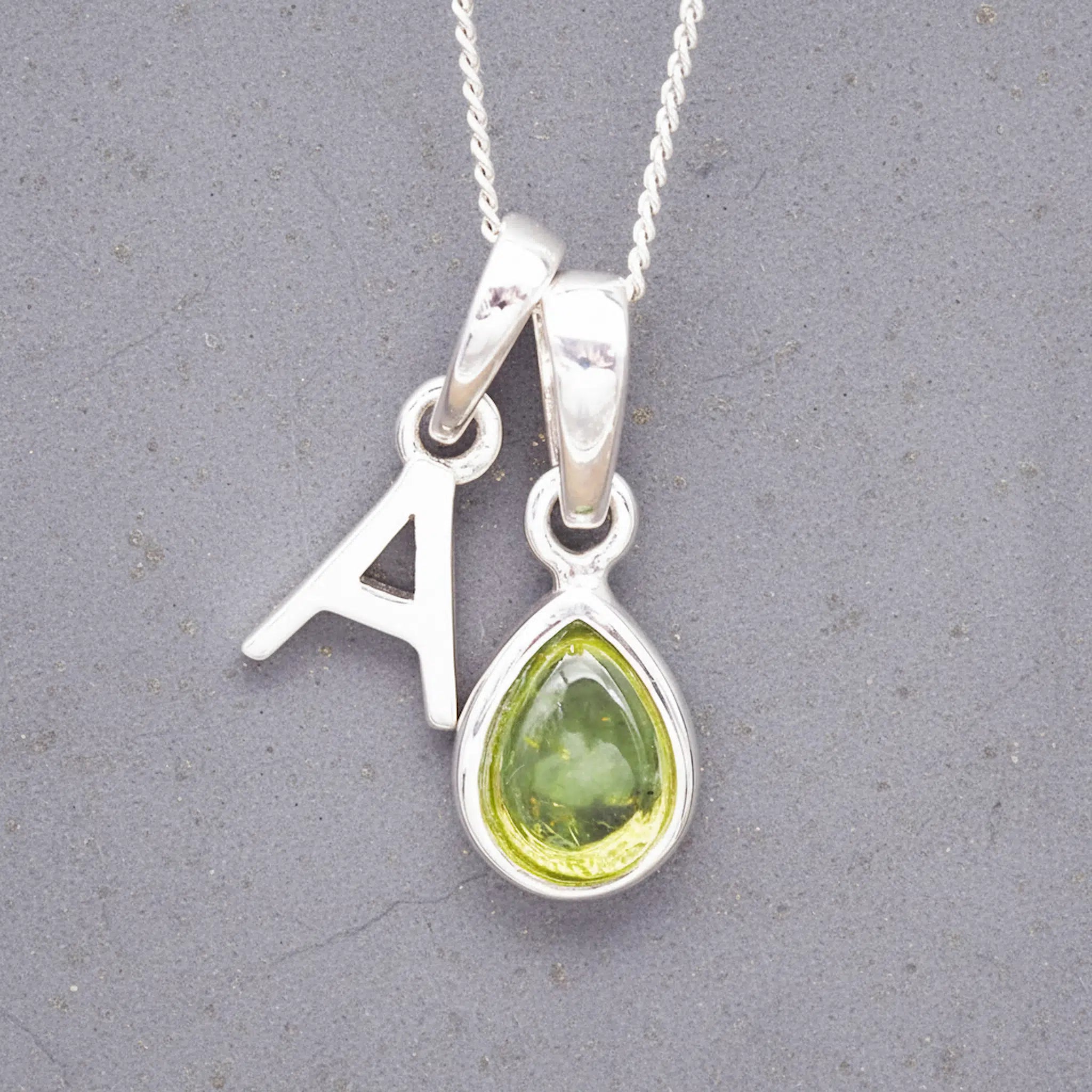 sterling Silver double pendant necklace with a green teardrop august birthstone peridot pendant and letter 'A' charm on a grey background