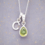 Sterling Silver 'C' Initial Necklace with a pear-shaped cabochon August Birthstone Peridot Pendant on a grey background