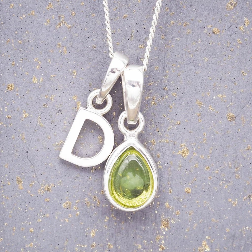 Sterling Silver 'D' Initial Necklace with a pear-shaped cabochon August Birthstone Peridot Pendant on a grey background