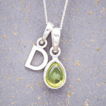Sterling Silver 'D' Initial Necklace with a pear-shaped cabochon August Birthstone Peridot Pendant on a grey background