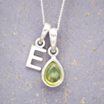 Sterling Silver 'E' Initial Necklace with a pear-shaped cabochon August Birthstone Peridot Pendant on a grey background