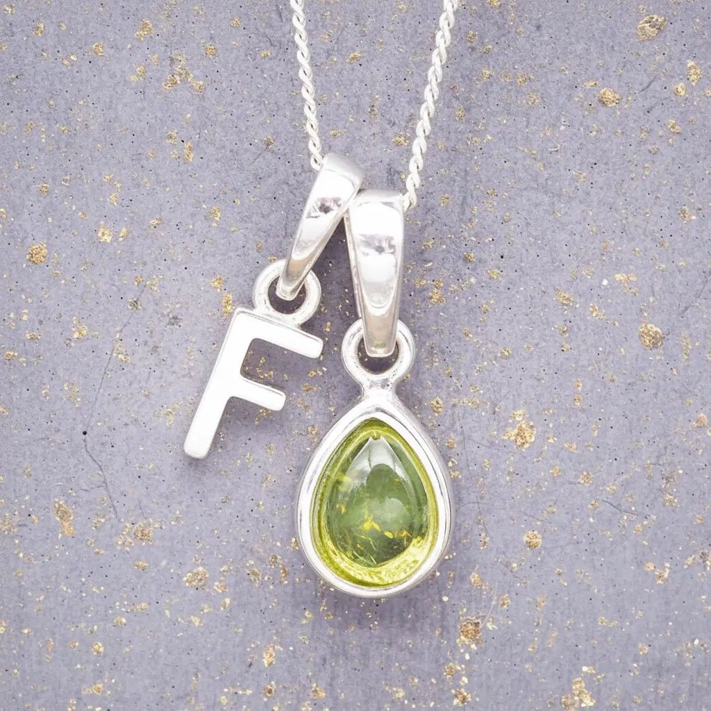 Sterling Silver 'F' Initial Necklace with a pear-shaped cabochon August Birthstone Peridot Pendant on a grey background