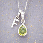 Sterling Silver 'F' Initial Necklace with a pear-shaped cabochon August Birthstone Peridot Pendant on a grey background