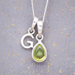 Sterling Silver 'G' Initial Necklace with a pear-shaped cabochon August Birthstone Peridot Pendant on a grey background