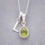 Sterling Silver 'L' Initial Necklace with a pear-shaped cabochon August Birthstone Peridot Pendant on a grey background
