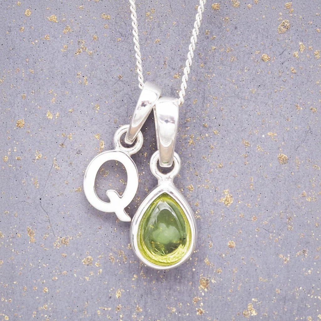 Sterling Silver 'Q' Initial Necklace with a pear-shaped cabochon August Birthstone Peridot Pendant on a grey background