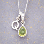 Sterling Silver 'Q' Initial Necklace with a pear-shaped cabochon August Birthstone Peridot Pendant on a grey background