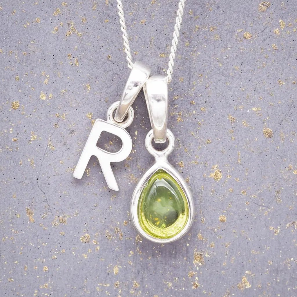 Sterling Silver 'R' Initial Necklace with a pear-shaped cabochon August Birthstone Peridot Pendant on a grey background