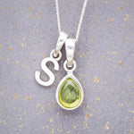 Sterling Silver 'S' Initial Necklace with a pear-shaped cabochon August Birthstone Peridot Pendant on a grey background