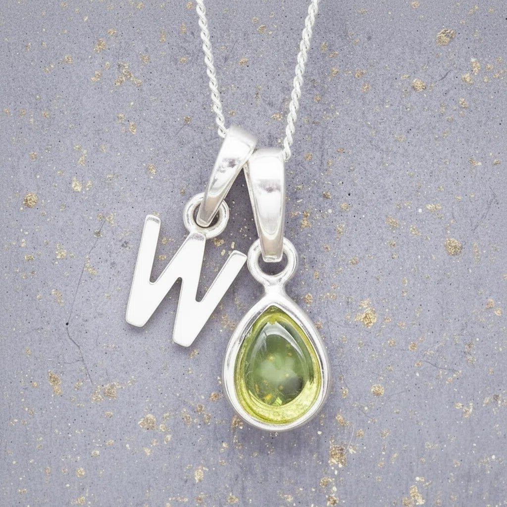Sterling Silver 'W' Initial Necklace with a pear-shaped cabochon August Birthstone Peridot Pendant on a grey background