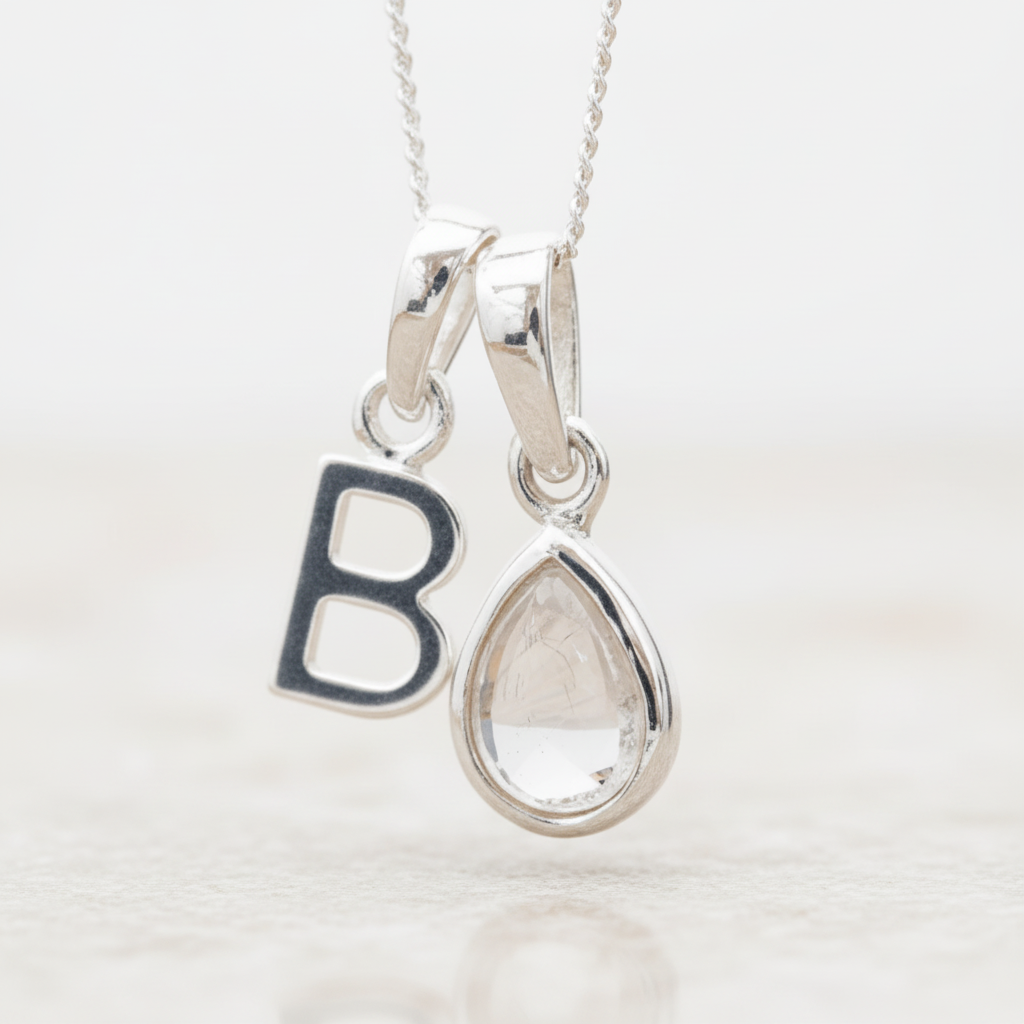 Silver Initial B necklace with a teardrop-shaped Herkimer Quartz crystal pendant hanging above a rustic wooden surface