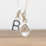 Silver Initial B necklace with a teardrop-shaped Herkimer Quartz crystal pendant hanging above a rustic wooden surface