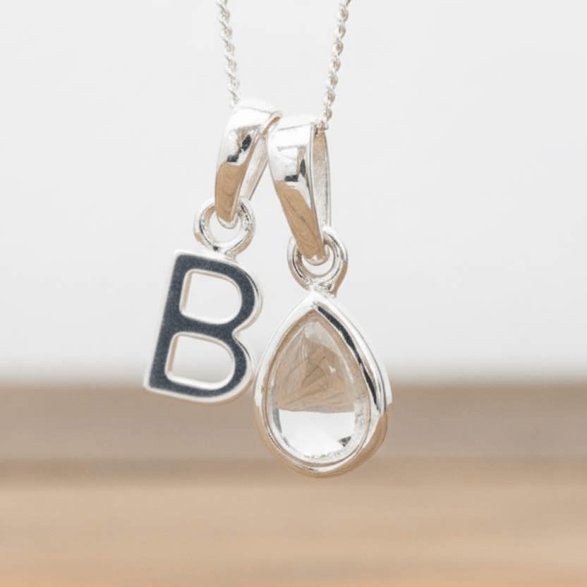 Silver Initial B necklace with a teardrop-shaped Herkimer Quartz crystal pendant hanging above a rustic wooden surface