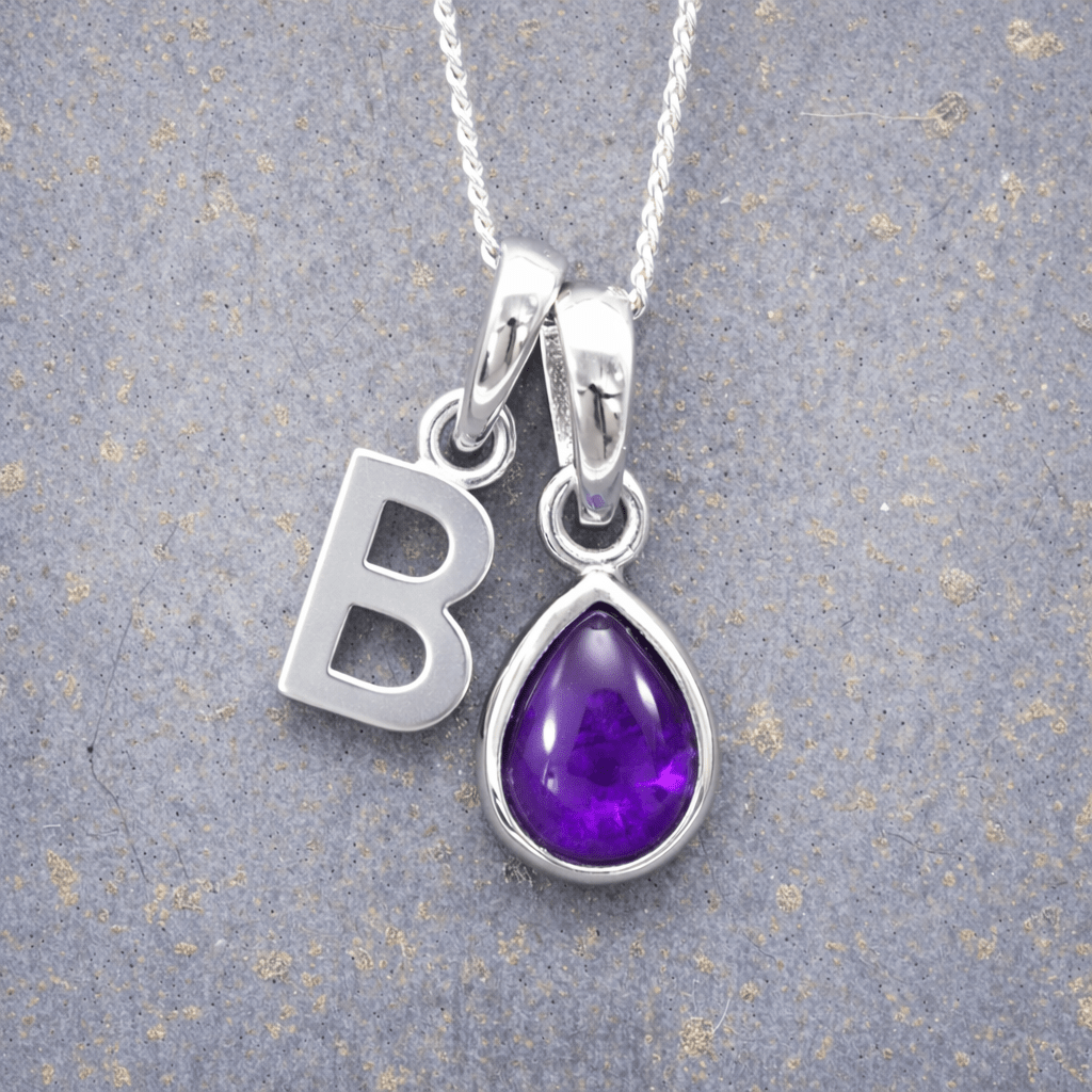 Silver necklace with 'B' initial pendant and purple teardrop february birthstone amethyst gemstone charm on a textured grey background