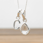 Silver Initial C necklace with a teardrop-shaped Herkimer Quartz crystal pendant hanging above a rustic wooden surface