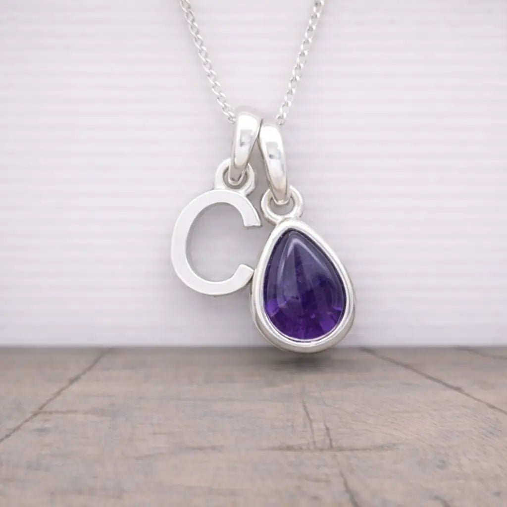 Silver initial c necklace with a teardrop-shaped purple amethyst gemstone pendant on a wooden surface.