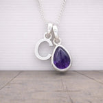 Silver initial c necklace with a teardrop-shaped purple amethyst gemstone pendant on a wooden surface.