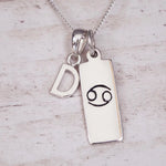 Sterling Silver necklace with 'D' initial pendant and Cancer Zodiac pendant on a textured grey background.
