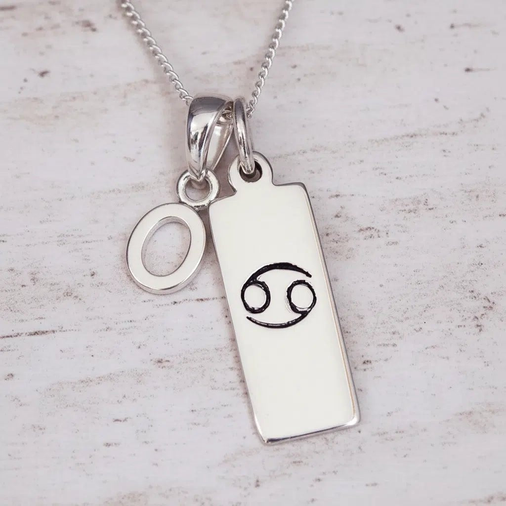 Sterling Silver necklace with 'O' initial pendant and Cancer Zodiac pendant on a textured grey background.