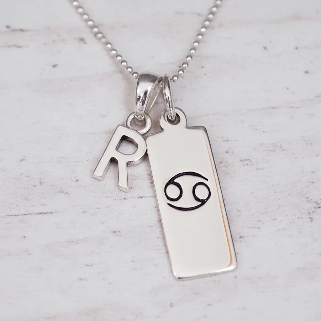 Sterling Silver necklace with 'R' initial pendant and Cancer Zodiac pendant on a textured grey background.