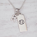 Sterling Silver necklace with 'R' initial pendant and Cancer Zodiac pendant on a textured grey background.