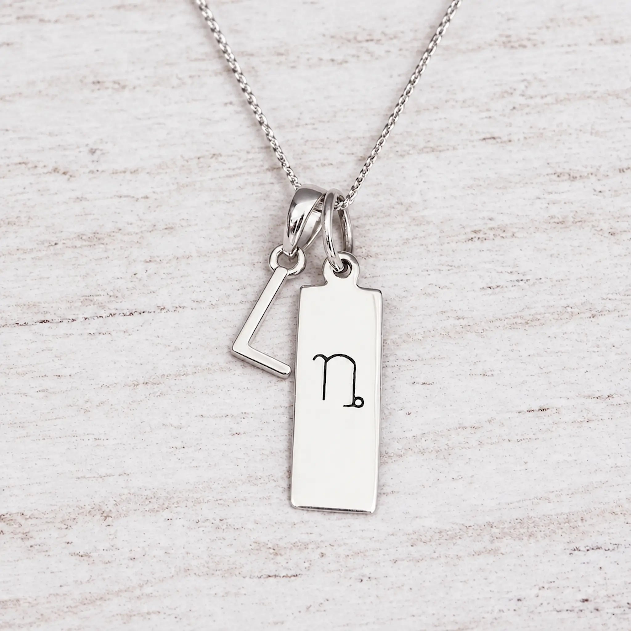 Silver Initial and Capricorn Zodiac Necklace with sterling silver letter L pendant on light wood